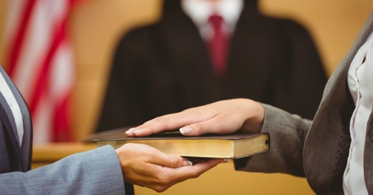 Selective focus photo of a person's hand on the bible while getting sworn-in in court.