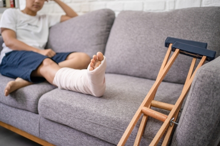 Young woman with a broken leg sitting on the sofa.